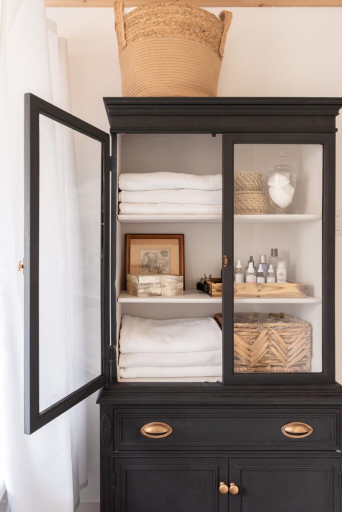 black wooden display cabinet with glass doors containing guest bathroom supplies