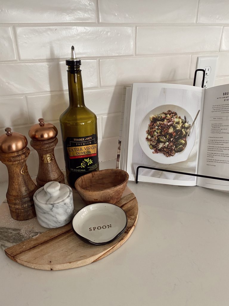 Wood round tray with salt, paper, olive oil bottle and ceramic spoon rest on top of it