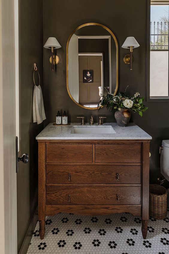 bathroom vanity with gold mirror, wall-mounted sconces and a potted plant