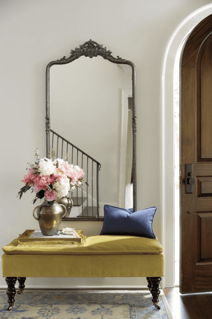 Photo of a velvet yellow bench with a vintage mirror providing an example of a classy, girly small entryway idea 