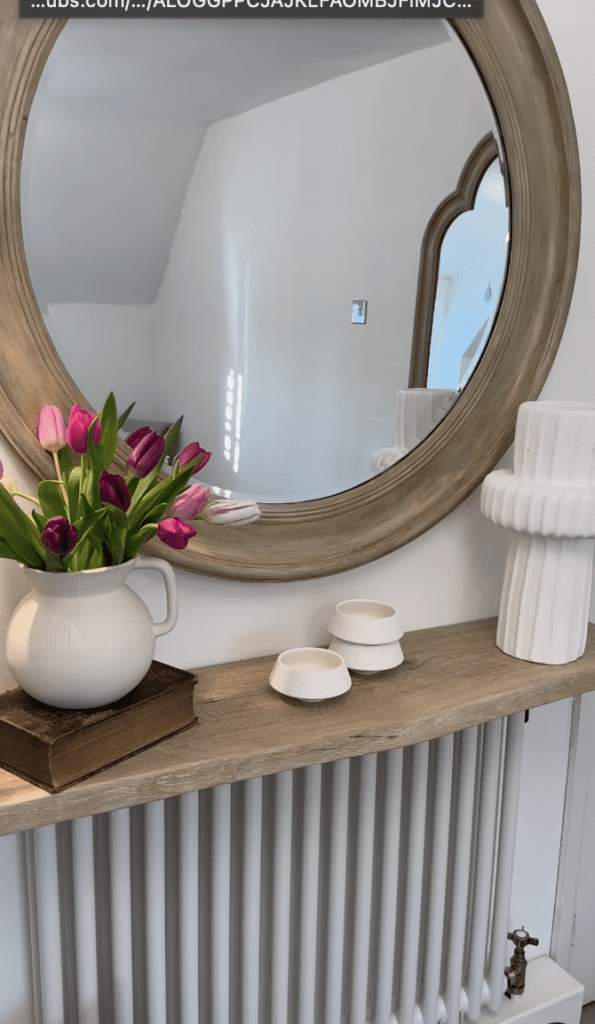 Entryway wooden shelf built on top of a radiator with a round large mirror and flowers