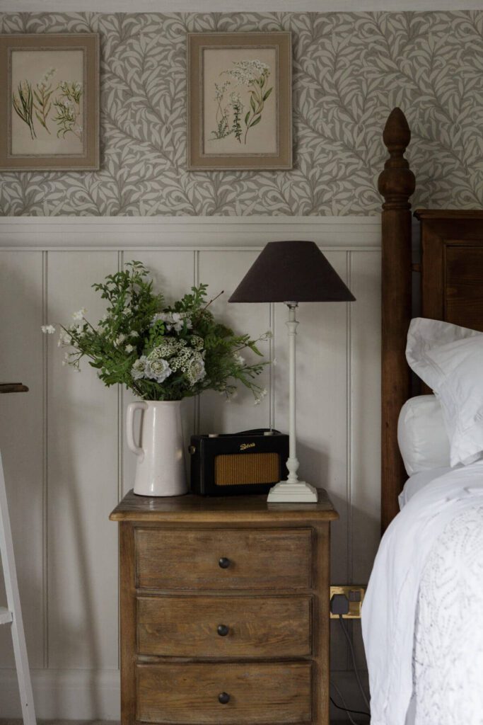 Small solid wood bedside table styled with a white vase filled with flowers and a vintage music player