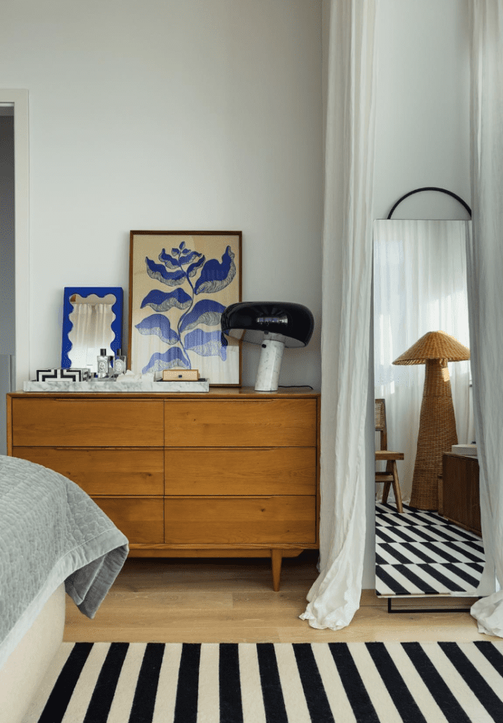 Mid century dresser with beautiful decor and a full body mirror leaning against classic white curtains