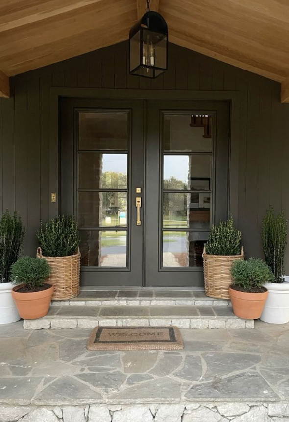 entry door with evergreen plants and variety of planters