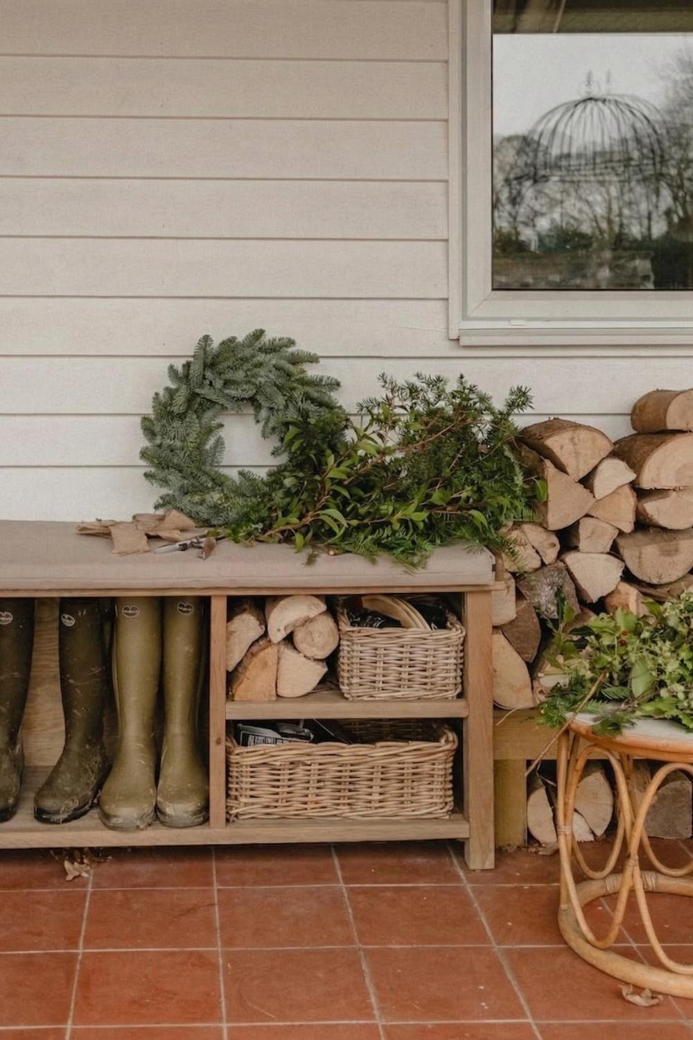 Functional cottage mudroom porch with a white wood exterior, green boots, and a bench filled with stacked firewood.