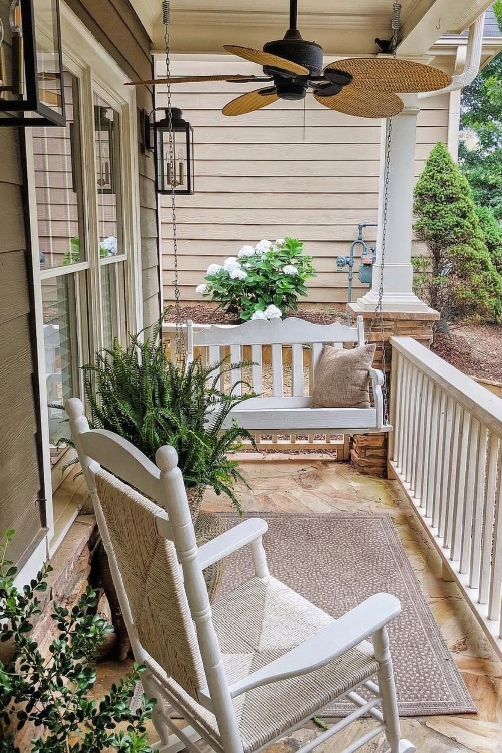 Traditional white farmhouse porch idea with a white rocking chair, ceiling fan, and neutral outdoor rug for a clean cottage aesthetic.