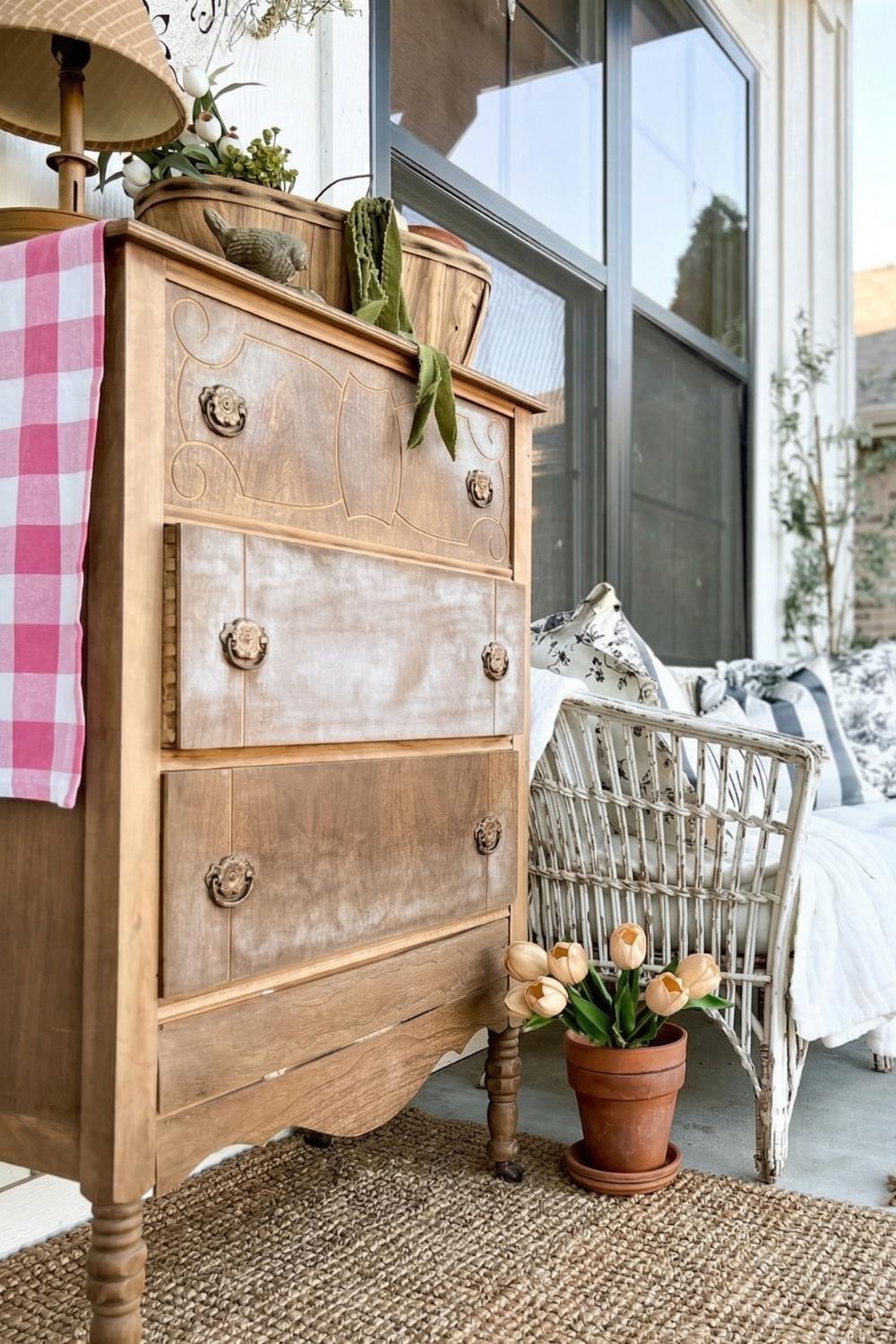 Antique wooden dresser on a cottage porch styled with a pink checkered cloth and terracotta potted tulips.